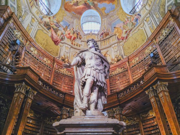 Marble statue of Emperor Charles VI under the frescoed dome of the State Hall (Prunksaal) in the Austrian National Library, Vienna, with walnut bookcases rising on every side