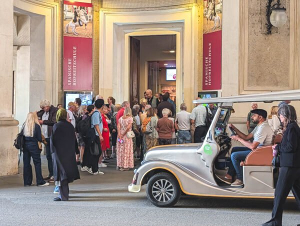 Tourists queue at the Spanish Riding School entrance at Hofburg, with red Spanische Hofreitschule banners